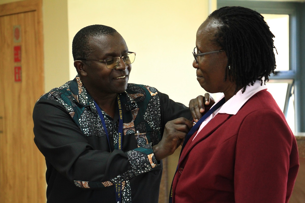 Prof. Munyae Mulinge pins a QM badge onto Prof. Juliana Namada, one of the QM Ambassadors during the event, which saw 90 faculty members receive their certificates for completion of the Quality Matters training. Photo: Jemima Oloo